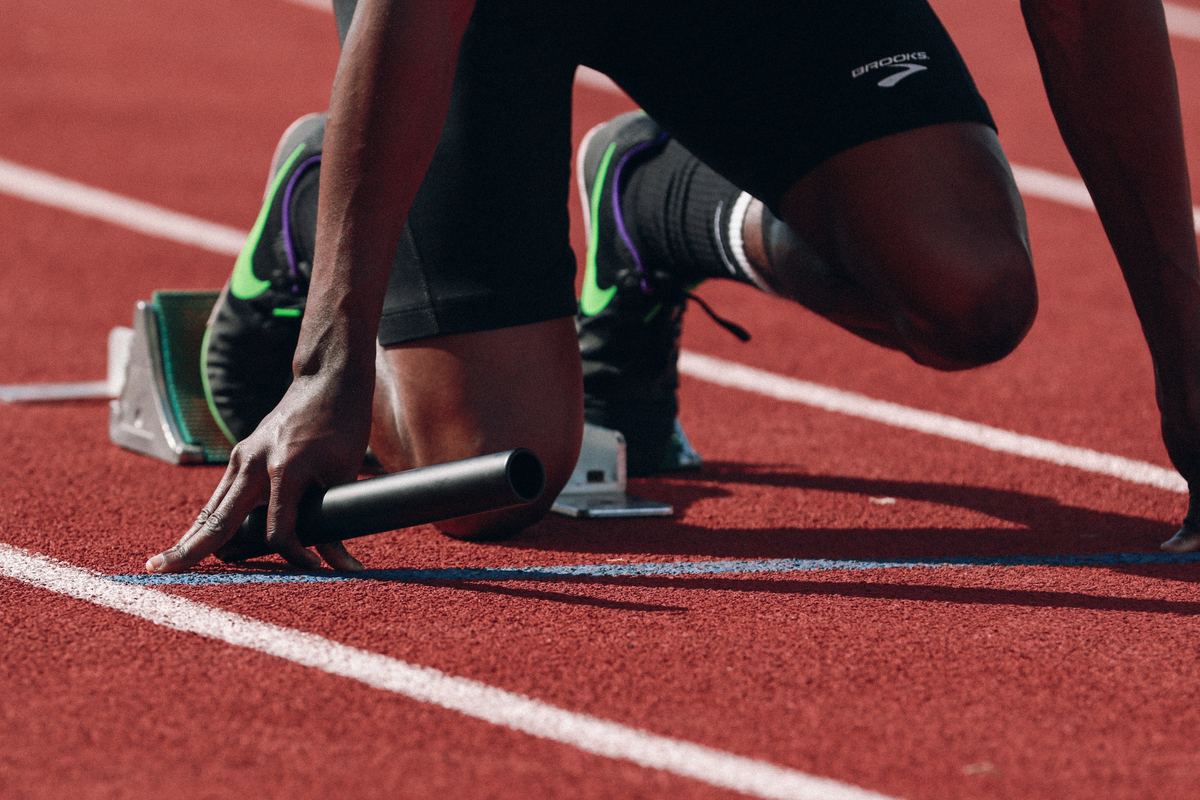 A sprinter set in the starting blocks, hand on the baton